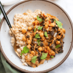 Bowl of miso peanut chickpeas and brown rice on a marble countertop and green cloth.
