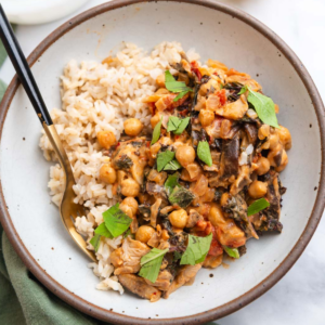Bowl of miso peanut chickpeas and brown rice on a marble countertop and green cloth.