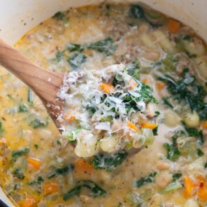 Ladle of soup topped with grated Parmesan with more soup in the background.