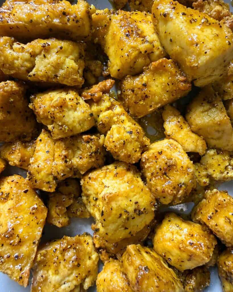 Close up of crispy tofu chunks coated in lemon pepper sauce.