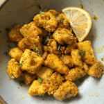 Gray bowl with a wedge of lemon and crispy nuggets of tofu in lemon pepper sauce.