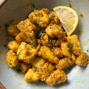 Gray bowl with a wedge of lemon and crispy nuggets of tofu in lemon pepper sauce.