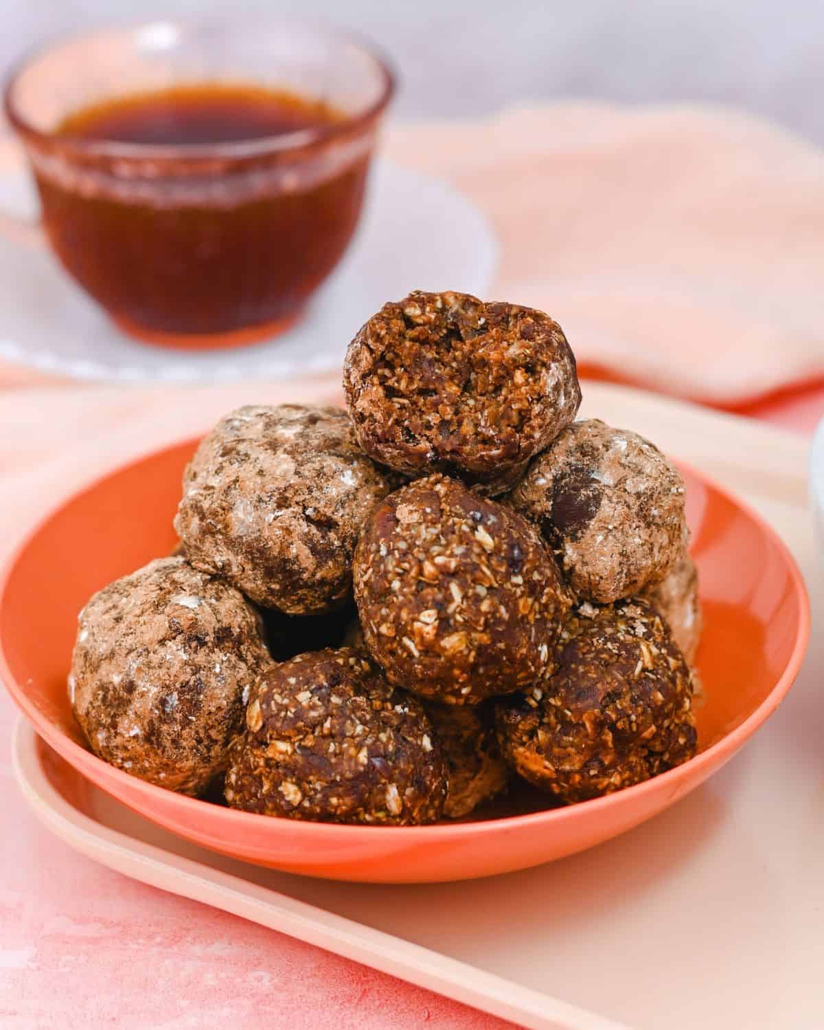 Pile of energy balls in a pink bowl with the top ball with a bite taken out of it.