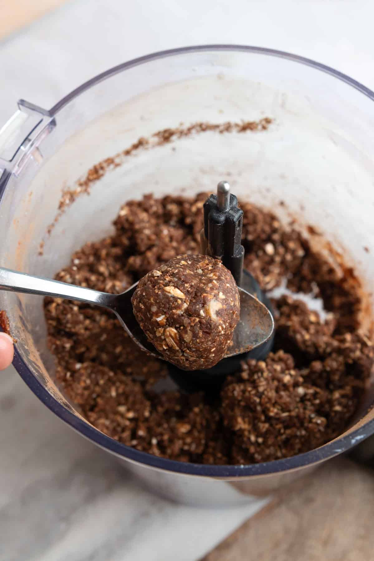 Spoon lifting a ball of energy bite batter out of the food processor.